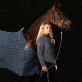 Seitenansicht braunes Pferd mit Abschwitzdecke Fleece Stamp mit Halfter und Führstrick in der Kollektionsfarbe doveblue wird von weiblichen, blonden Model mit farblich passender Jacke geführt, Hintergrund schwarz.