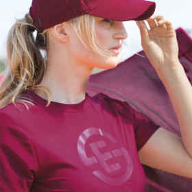 Seitliche Nahaufnahme weibliches, blondes Model mit T-Shirt Tech Jersey in der Kollektionsfarbe berryfusion und der farblich passenden Cap in berryfusion. Hintergrund Natur.