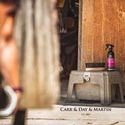 Image Bild: Canter Mane & Tail Sprühflasche 500 ml mit Label in pink steht neben einer Fellpflegebürste auf einem Schemel vor dem Stall.